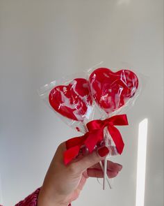 a person holding two lollipops wrapped in cellophane and tied with a red bow