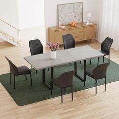 a dining room table with four chairs and a vase of flowers on the rug in front of it