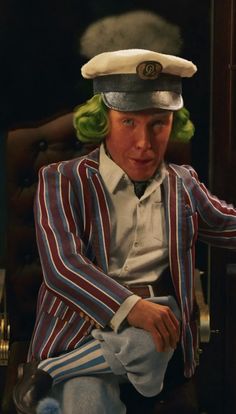 a man with green hair sitting in a chair wearing a sailor's hat and striped jacket