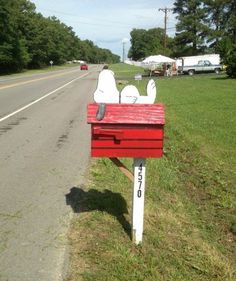 a red mailbox sitting on the side of a road next to a green field