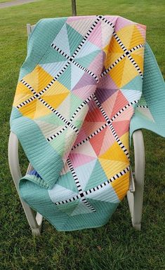 a quilt sitting on top of a lawn chair in the middle of a grass field