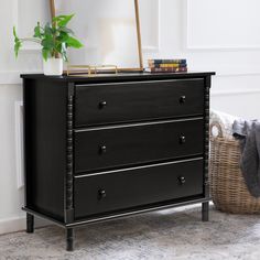 a black dresser with three drawers and a mirror on top of it next to a basket