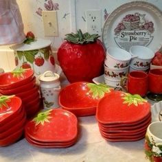 a table topped with lots of red plates and bowls filled with strawberries on them