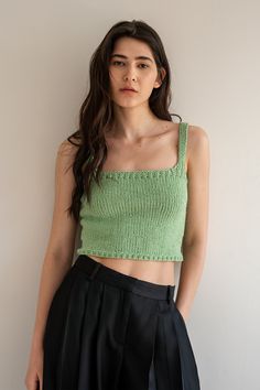 a woman wearing a green crop top and black pleated skirt standing in front of a white wall