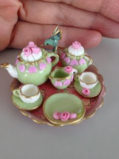 a miniature tea set with pink flowers on it in someone's hand, next to some cups and saucers