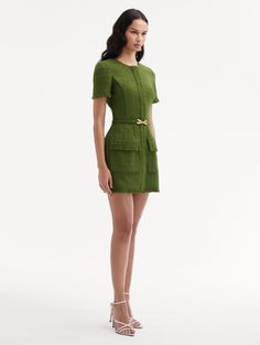 a woman wearing a green dress and heels standing in front of a white background with her hands on her hips