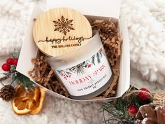 an open gift box containing a candle, orange slice and christmas decorations on a white blanket