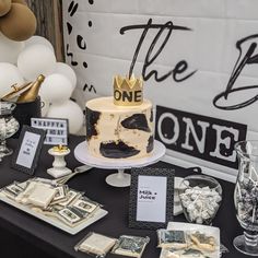 a table topped with a cake covered in gold and black frosting next to balloons