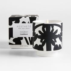 a candle that is next to a box on a white surface with black and white designs