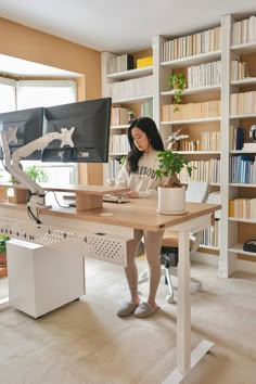 a woman sitting at a desk in front of a computer monitor and bookshelf