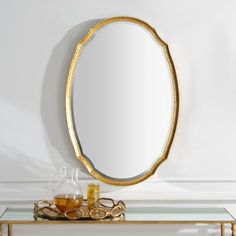 an oval mirror sitting on top of a table next to a vase and glass bottle