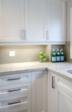 a kitchen with white cabinets and marble counter tops is pictured in this image, there are several bottles on the counter