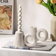 two white vases sitting on top of a table next to a candle and some flowers