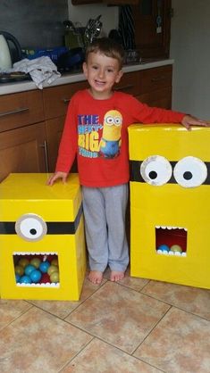 a young boy standing next to two cardboard boxes with eyes and mouths painted on them