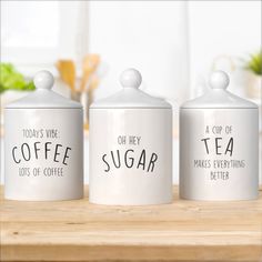 three white canisters with words on them sitting on a wooden table next to a potted plant