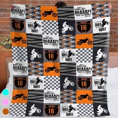 a blanket with an orange and black motorcycle design on it, hanging up against a brick wall