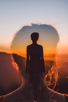 a woman standing on top of a mountain with her hair blowing in the wind at sunset