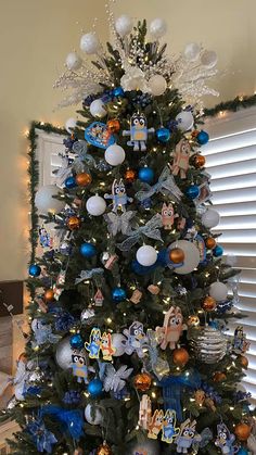 a decorated christmas tree with blue and silver ornaments on it's branches in front of a window