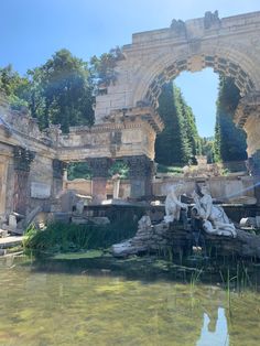 an arch in the middle of a body of water with statues on it and trees around