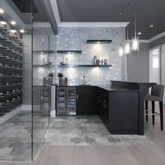 a modern kitchen with black cabinets and glass wine racks on the wall behind the bar