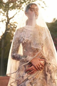 a woman in a wedding dress with a veil over her head and hands on her chest