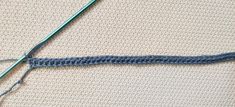 a blue crochet stitch on the side of a piece of fabric with a green knitting needle next to it