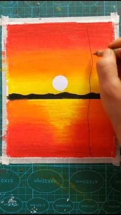 someone is painting an orange and yellow sunset on a piece of paper with a pencil