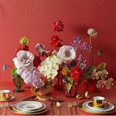 a red table topped with plates and vases filled with different types of flowers next to each other