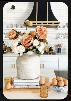 an arrangement of flowers in a vase on top of some books and eggs sitting on a kitchen counter