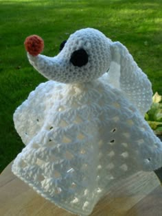 a white crocheted stuffed animal with an apple in it's mouth sitting on top of a wooden table