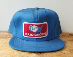 a blue hat with the words mr automote on it sitting on top of a wooden table