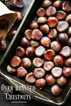 roasted chestnuts in baking pan on wooden table with pine cones and paper towel next to them