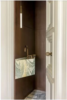 an open door leading to a bathroom with marble counter tops and wooden walls, along with a gold faucet