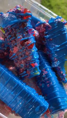 two blue plastic cups filled with different types of colored sand and seaweed in water