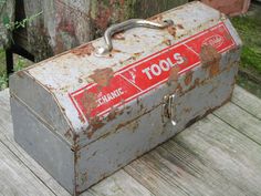 an old metal tool box sitting on top of a wooden table next to a fence