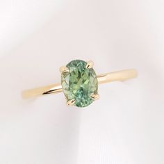 a ring with a green stone in the center on a white surface, it is gold and has a thin band