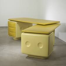 a yellow desk with two drawers on each side and a white wall in the background