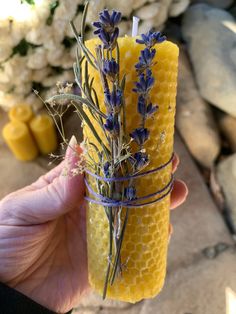 a hand holding a small candle with lavender on it and some flowers in the middle