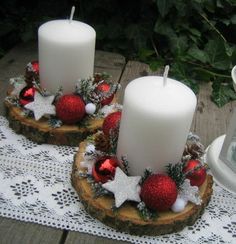 two white candles sitting on top of wooden slices covered in christmas balls and ornaments next to a lit candle