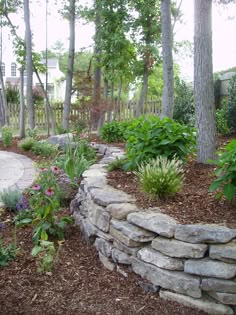 a stone wall surrounded by trees and flowers