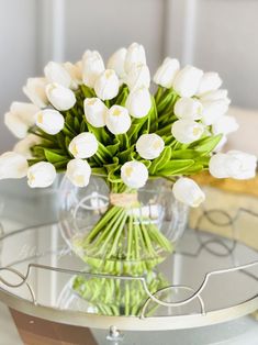 white tulips are arranged in a clear vase on a glass table with wire