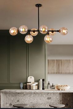 a kitchen with green walls and marble counter tops, lights above the island in front of it