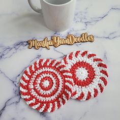 two crocheted coasters sitting on top of a table next to a coffee cup