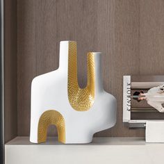 a white and gold vase sitting on top of a table next to a magazine rack