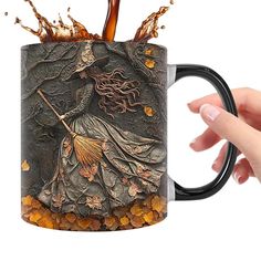 a hand holding a coffee mug with an image of a witch and leaves on it