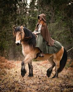 a woman riding on the back of a brown horse through a forest filled with trees