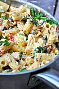 a pan filled with pasta and spinach on top of a wooden table