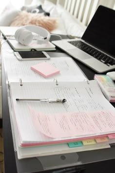 a laptop computer sitting on top of a desk next to a pile of papers and pens