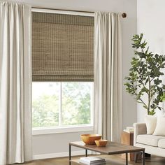 a living room with a couch, coffee table and window covered in bamboo roman shades