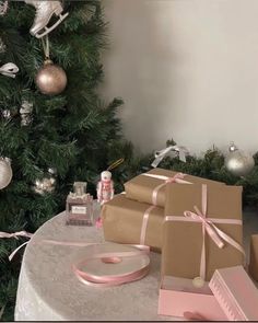 presents are on the table next to a christmas tree with pink ribbon and ornaments around it